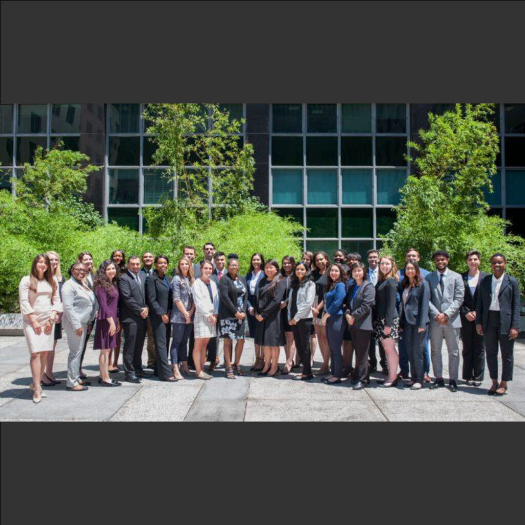 group photo of people in business attire standing in front of a building and trees